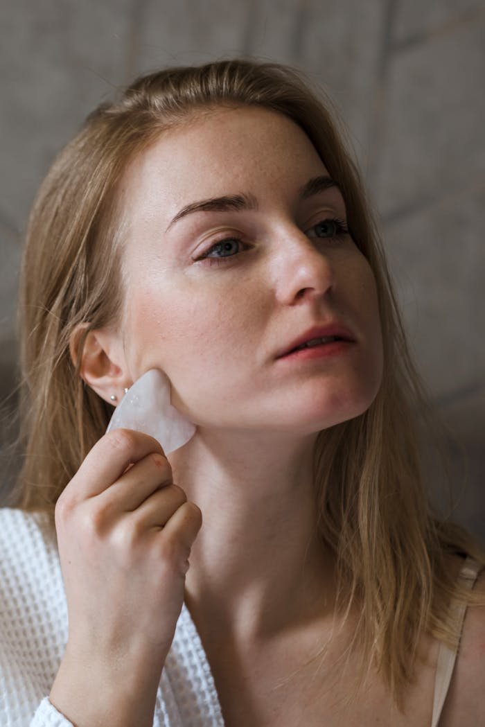A woman using a gua sha tool on her face for skincare routine, promoting wellness and self-care.